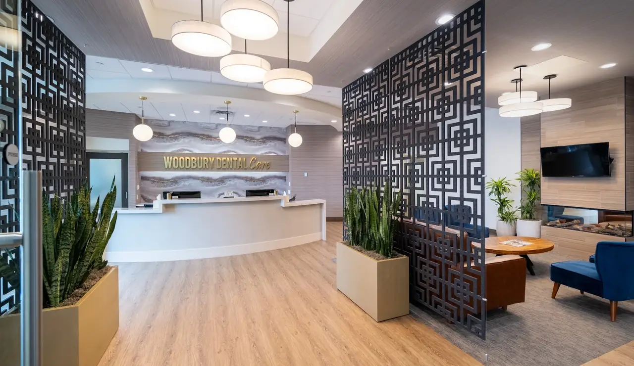 The reception desk at Woodbury Dental Care, with the practice's name in gold lettering, a patterned screen, and the fireside lounge beside it.