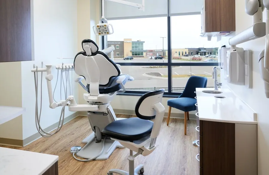 A treatment room at Woodbury Dental Care with a window, an ergonomic chair and a ceiling-mounted TV.